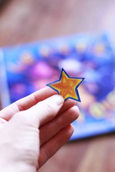 Hand holding a hand drawn yellow star with blurry book in the background.